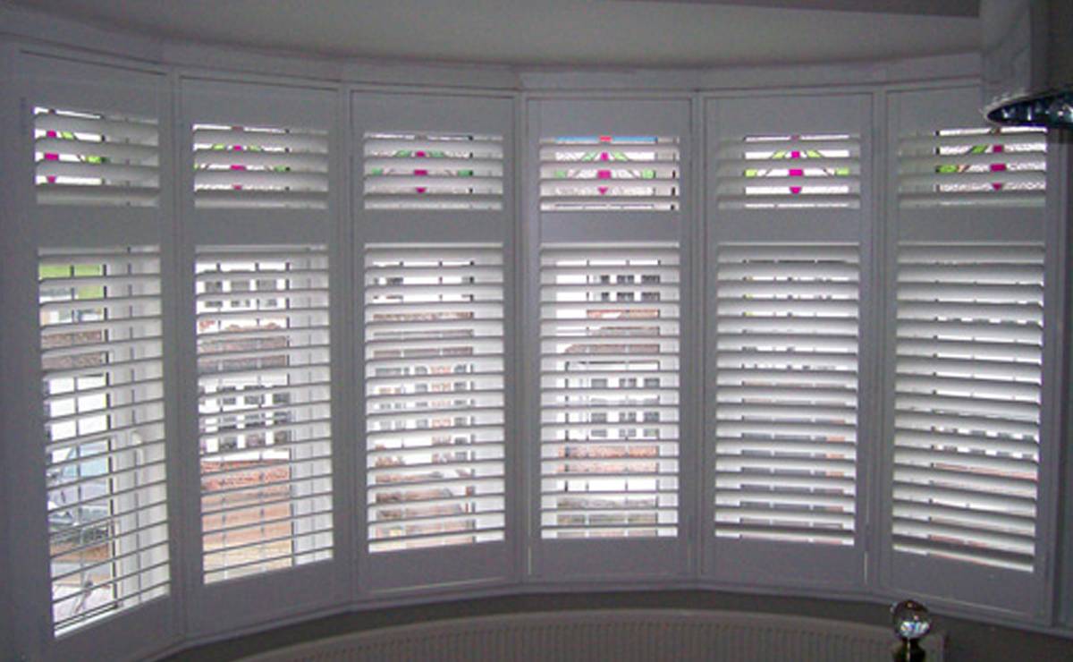 a bay window with white shutters in a bedroom